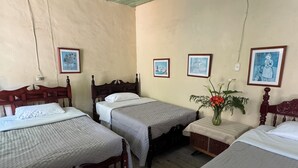 A room with three wooden beds, each with a white pillow and grey bedding. There is a small table with a vase of flowers and a framed picture on the wall. - Casa colonial con encanto en Sonsón (Sonsón)