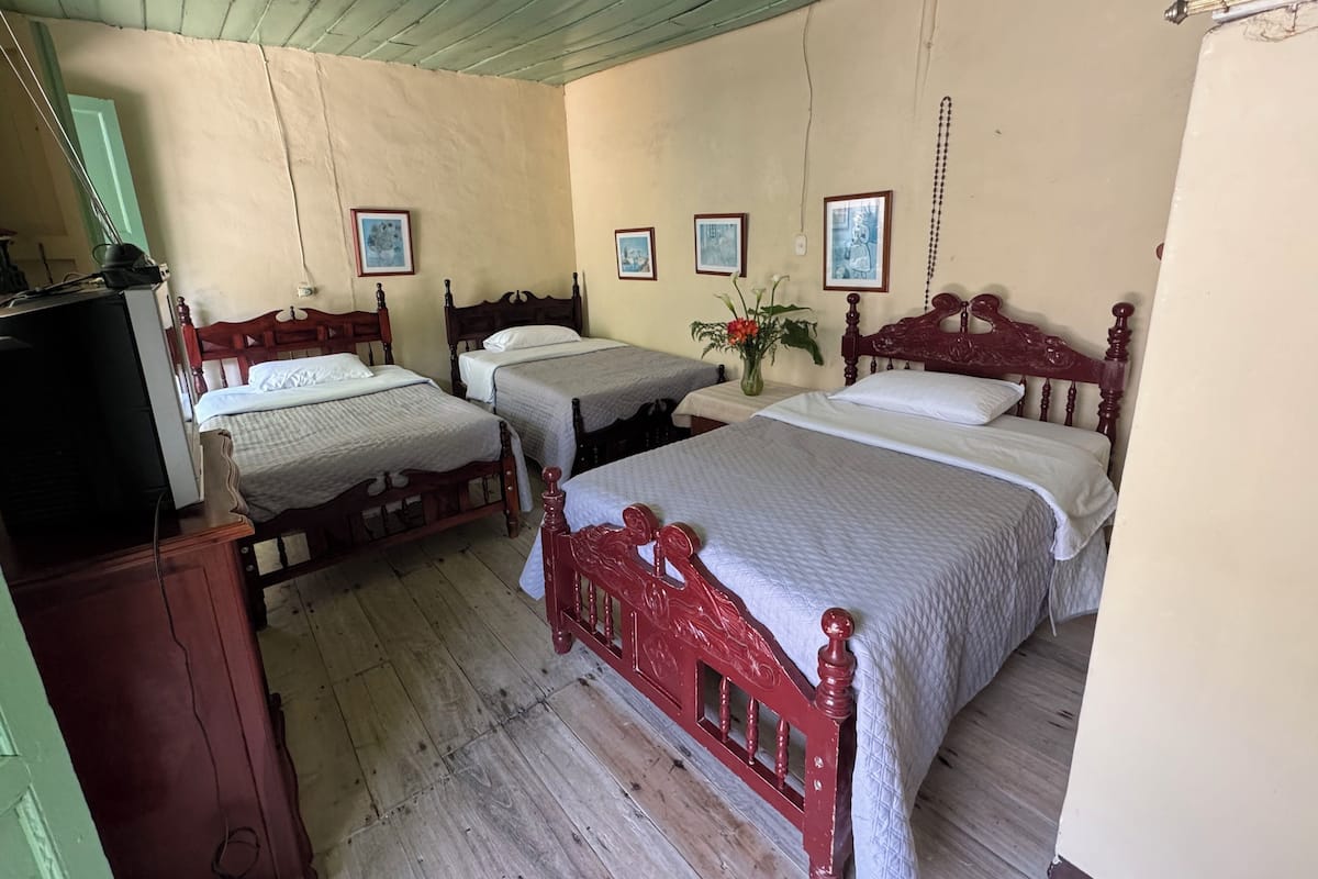 Una habitación con tres camas de madera, un televisor y cuadros enmarcados en la pared.