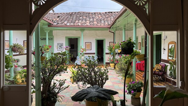 An open courtyard with a tiled floor, potted plants, and a view of a building with a tiled roof. - Casa colonial con encanto en Sonsón (Sonsón)