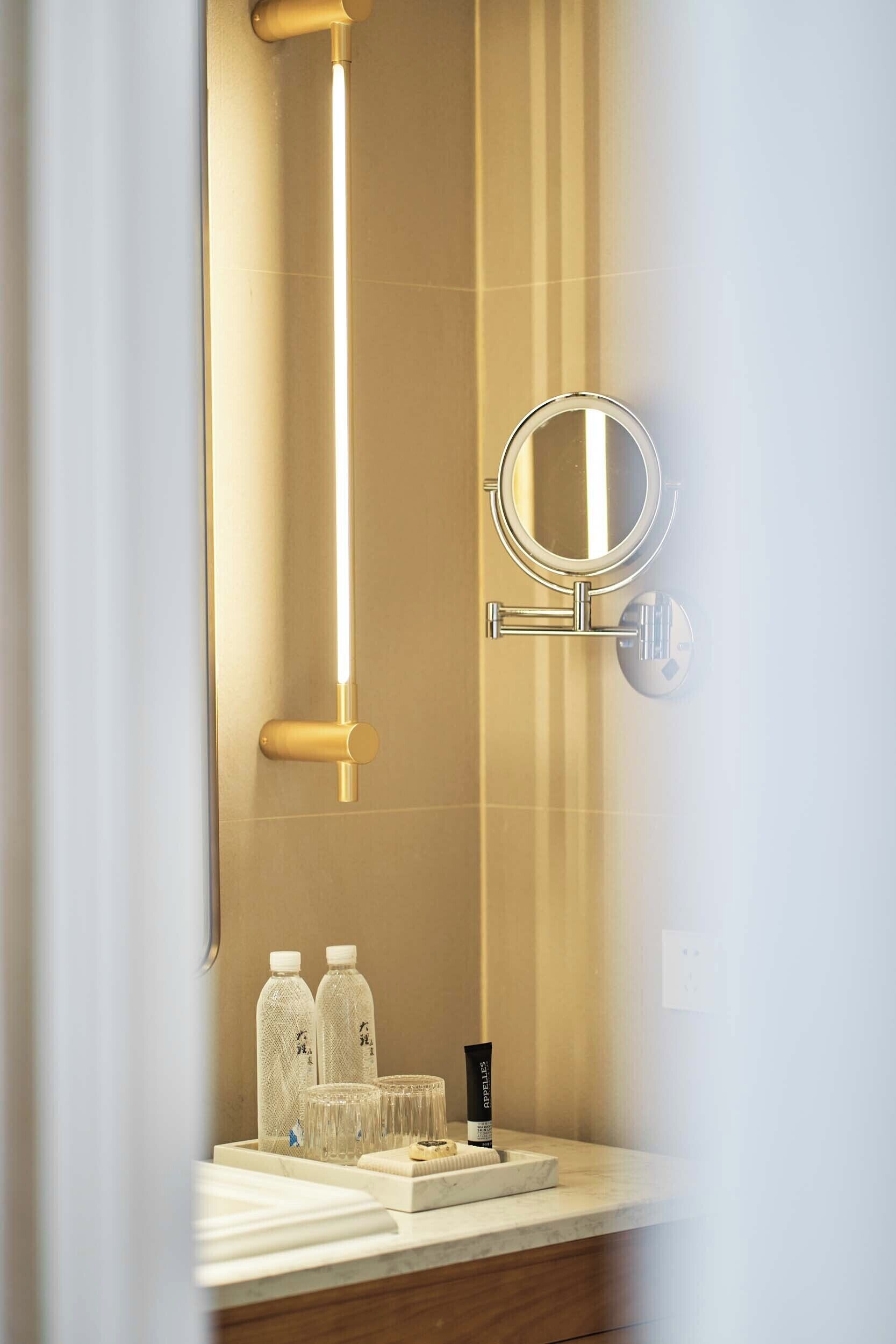 Un baño con diseño moderno, que incluye una lámpara vertical, un espejo redondo y artículos de tocador sobre la encimera.