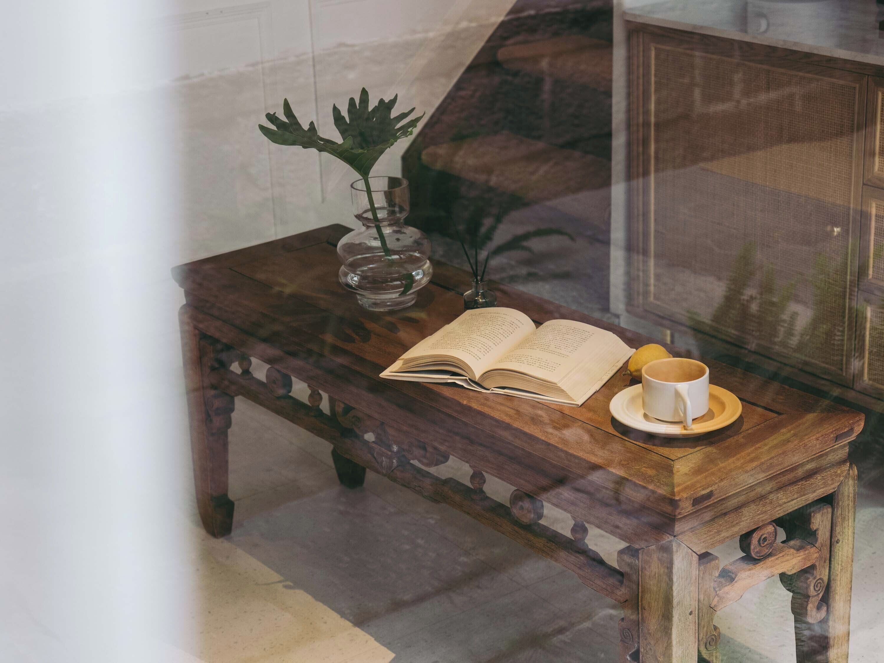 Un tavolo di legno con un libro, una tazza e un vaso con una pianta.