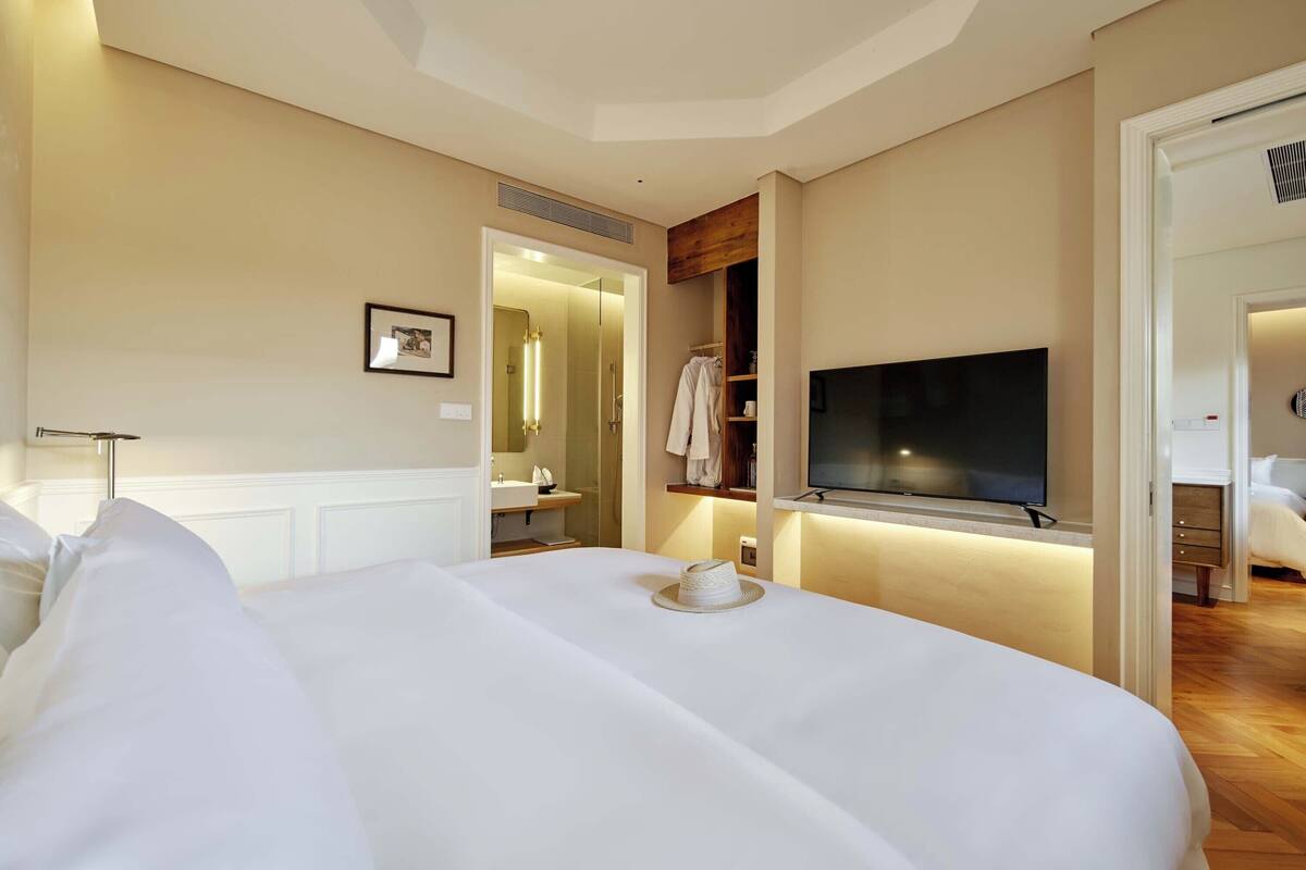 A hotel room with a large bed, a flat-screen TV mounted on the wall, a walk-in closet, and a bathroom with a mirror and sink.