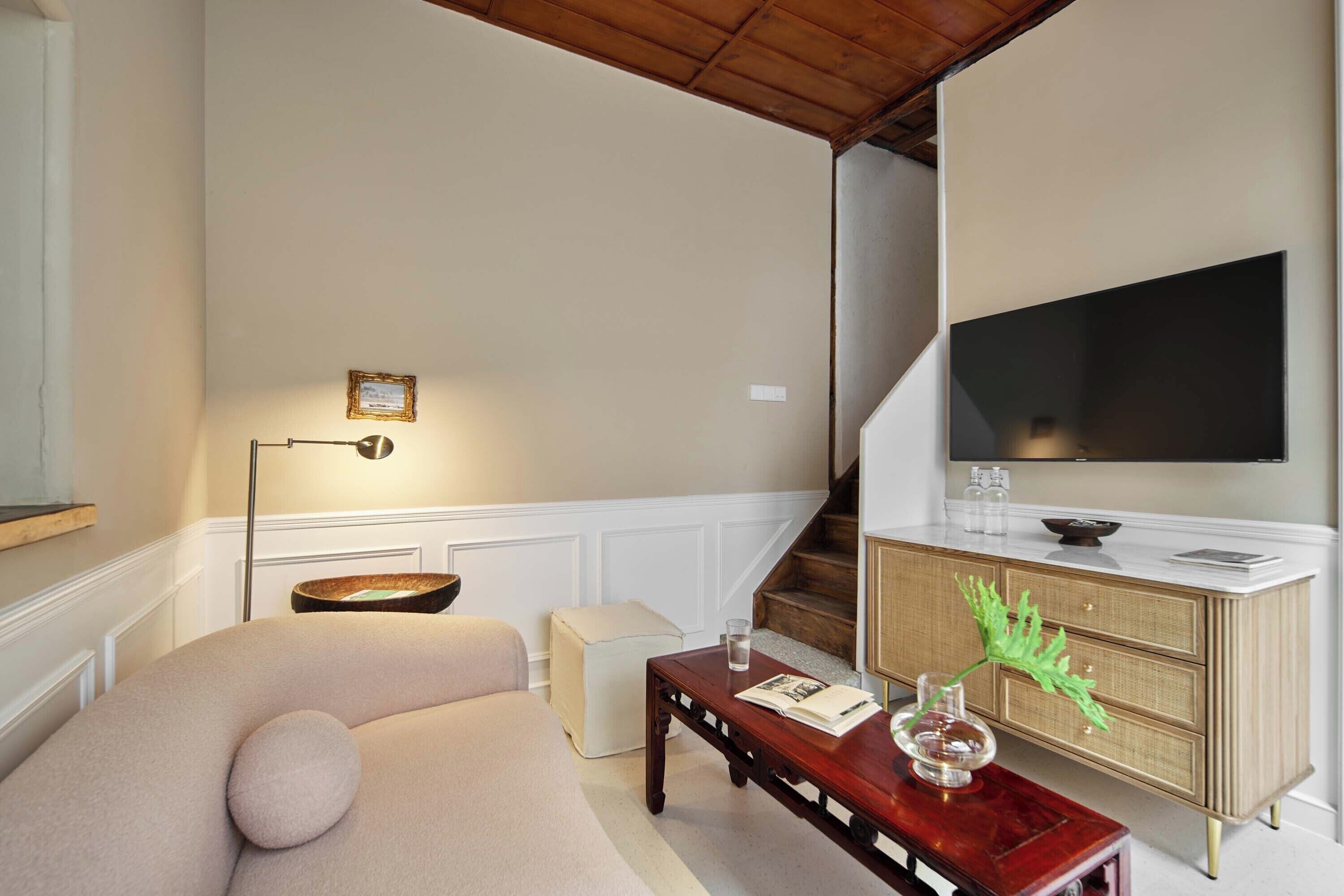 Een woonkamer met een bank, een salontafel, een televisie, een trap en een kast.