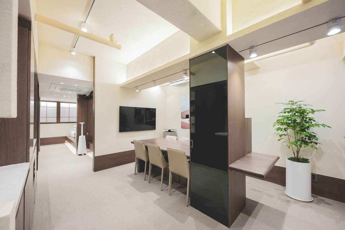 A modern conference room with a long table, four chairs, a flat-screen TV, and a potted plant.