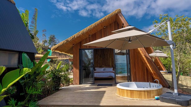 A modern, wooden cabin with a glass door leading to a bedroom, a hot tub, and an umbrella providing shade. - Wanluhu Xingyue Homestay (Heyuan)