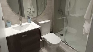 Un baño moderno con un espejo redondo, un lavabo, un inodoro y una ducha con cerramiento de vidrio.