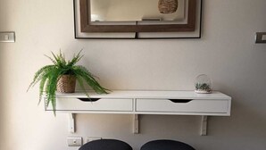 Una habitación moderna con una consola blanca, dos sillas negras, una planta en maceta y una lámpara colgante.