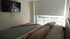 Un dormitorio con una cama, un televisor montado en la pared y una ventana con persiana.