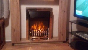 A fireplace with a TV on a stand to the right. - Wherry, pet friendly cottage. on the riverside with free fishing and mooring. (Wroxham)