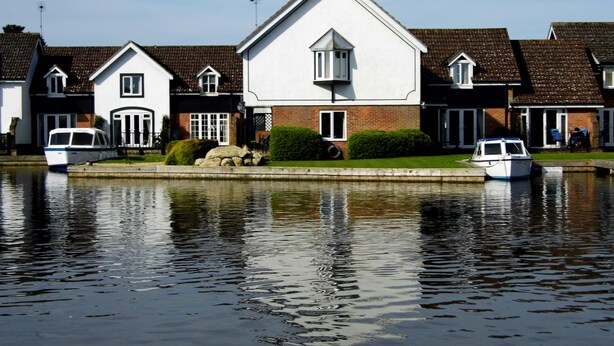 A row of houses by a calm water body with two boats docked. - Wherry, pet friendly cottage. on the riverside with free fishing and mooring. (Wroxham)