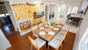 A dining area with a large wooden table set for six, surrounded by cushioned chairs. A map mural on the wall depicts Deland. - Minnesota Manor Home & Guest House-Your DeLand Getaway (DeLand)