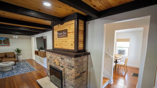 A living room with a fireplace, wooden ceiling beams, and a dining area with a table and chairs. - Minnesota Manor Home & Guest House-Your DeLand Getaway (DeLand)