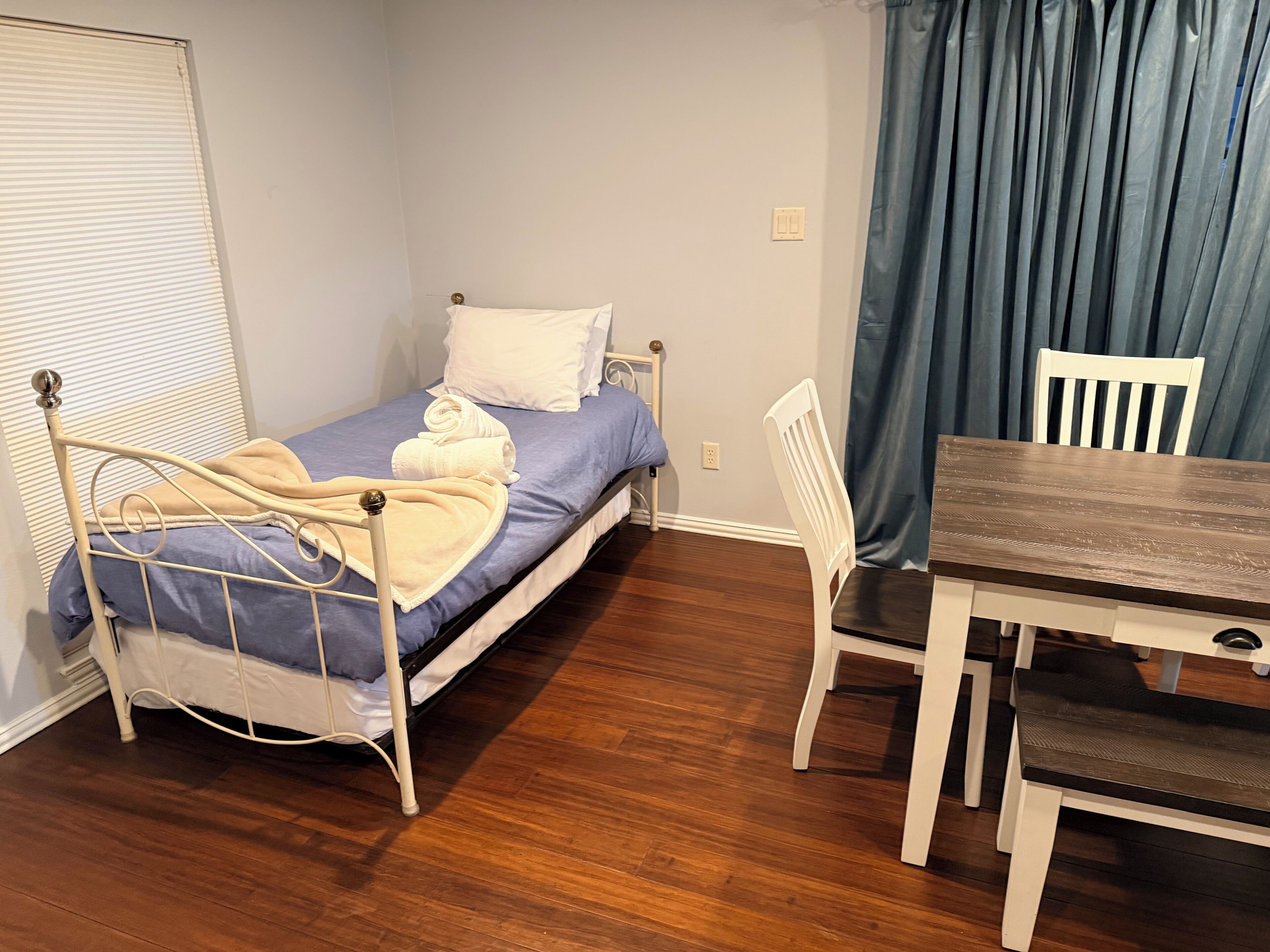 Una piccola stanza con un letto singolo, un tavolo di legno e una sedia.