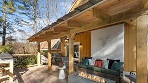 Eine Holzterrasse mit Feuerstelle, Sitzgelegenheiten im Freien und einem überdachten Bereich mit einer Couch und Sesseln.
