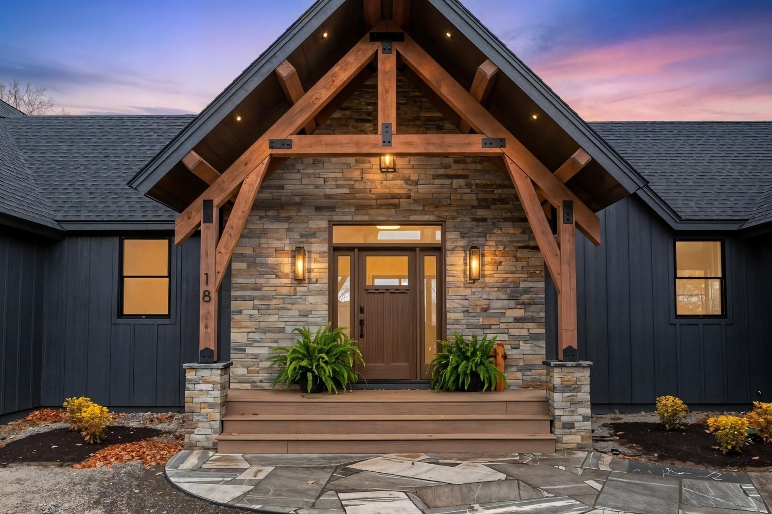 Une maison moderne avec une façade en pierre, des poutres en bois et un garage pour deux voitures.