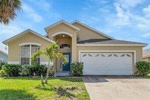 A single-story house with a garage, a front porch, and a small lawn. - Charming 5BR/4BA Near Disney/ Pool, Sauna & Pets (Kissimmee)