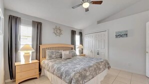 Ein Schlafzimmer mit Bett, Nachttischen, Deckenventilator, Tür und Wanduhr.