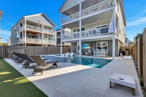 A two-story building with a pool, outdoor seating, and a wooden fence. - Hilton Head Coastal Compound Pool Putting Green (Hilton Head Island)