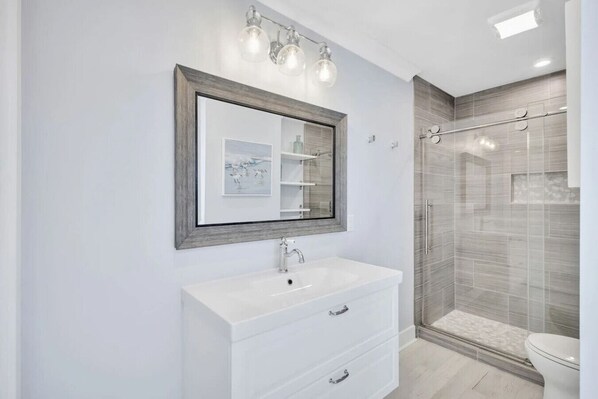A modern bathroom with a white vanity, a framed mirror, and a glass shower enclosure. - Hilton Head Coastal Compound Pool Putting Green (Hilton Head Island)