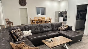 A modern living room with a sectional sofa, a coffee table, and a dining area with a table and chairs. - Enjoyable 4 Bedroom on M22 - Close to Traverse City & Suttons Bay (Traverse City)