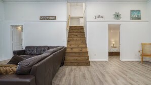 A spacious living area with a brown leather couch, a wooden staircase, and a wooden bench. - Enjoyable 4 Bedroom on M22 - Close to Traverse City & Suttons Bay (Traverse City)