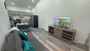 Uma sala de estar moderna com um sofá cinzento, almofadas verde-água, uma televisão de tela plana e um móvel de entretenimento de madeira.