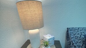 Uma mesa de cabeceira com abajur, um controle remoto, uma pequena planta e uma caixa de lenços.