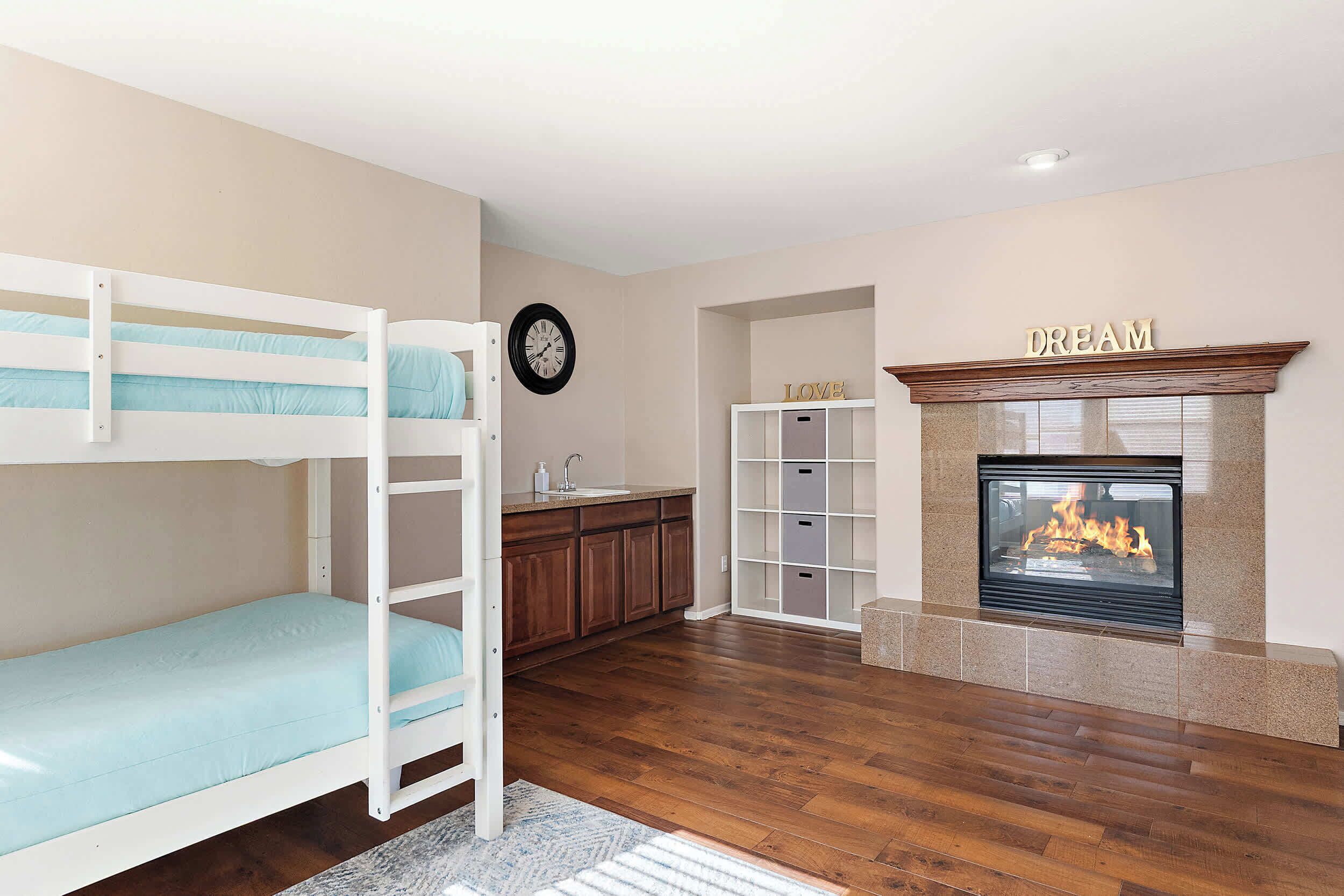 A room with bunk beds, a kitchen area, a fireplace, and a clock on the wall.