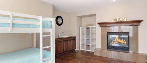 A room with bunk beds, a kitchen area, a fireplace, and a clock on the wall.