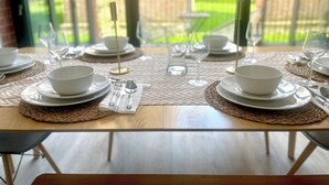 A dining table set for four with white plates, bowls, and cutlery, placed on a woven placemat. - Shoreditch Apartments by PrimeCityHosts F11 (Greater London)
