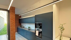 A modern kitchen with dark cabinetry, a built-in oven, and a white countertop. - Shoreditch Apartments by PrimeCityHosts F11 (Greater London)