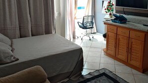 Una camera da letto con un letto, una poltrona, una scrivania con televisore e una finestra con tende.