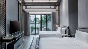 Una habitación de hotel moderna con una cama grande, un televisor de pantalla plana y un balcón con vistas a zonas verdes.
