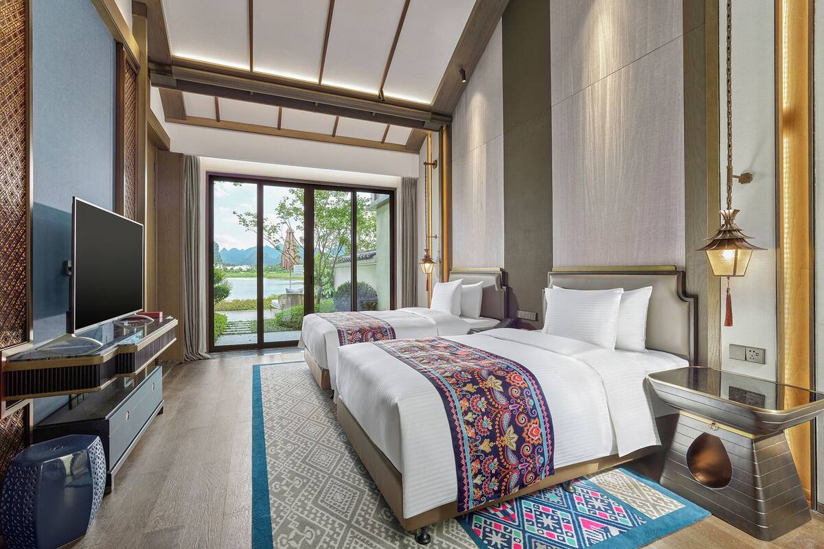 A hotel room with a large bed, a TV, a desk, and a view of a lake.