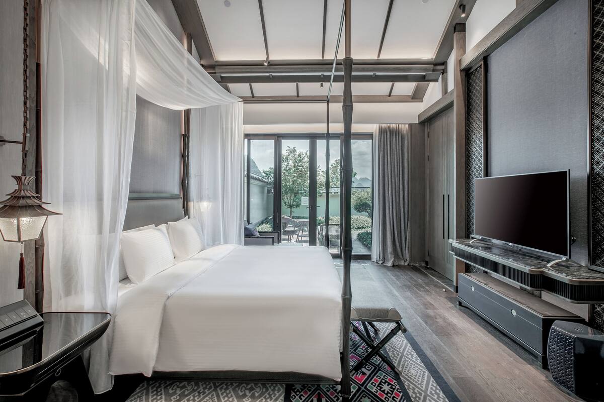 A modern hotel room with a large bed, a television, and a balcony with a view.