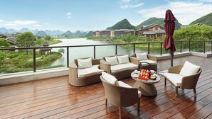A wooden deck with wicker furniture, a table with tea set, and a view of a river and mountains. - Song Hotel Guilin (Guilin)