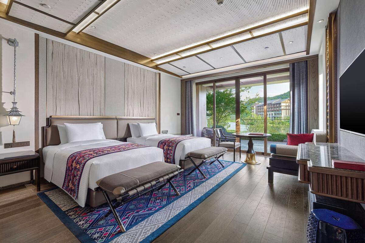 A hotel room with a large bed, a bench, a small table, and a TV.