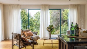 Ein Zimmer mit großem Fenster, einem Holzstuhl, einem kleinen Tisch und einer Vase mit Blumen.
