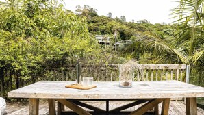 Eine Holzterrasse mit Tisch, umgeben von üppiger Vegetation und einer Hügelkulisse.