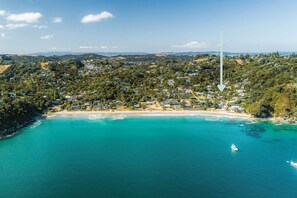 An aerial view of a coastal town with a beach, houses, and a boat in the water. - Miro Retreat – Sun-Soaked Palm Beach (Waiheke Island)