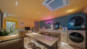 A modern kitchen with a neon sign, a dining area with a table and chairs, and a washing machine. - Sinchon APL Hotel (Seoul)