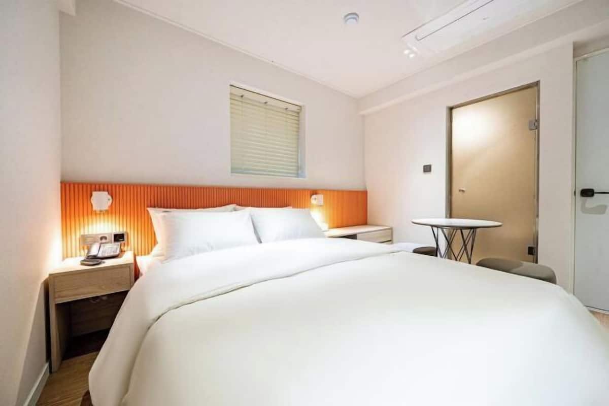 A hotel room with a bed, bedside table, lamp, and a small round table.