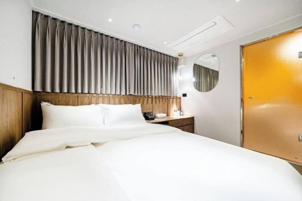 A hotel room with a bed, a wooden headboard, a nightstand, a mirror, and a door.
