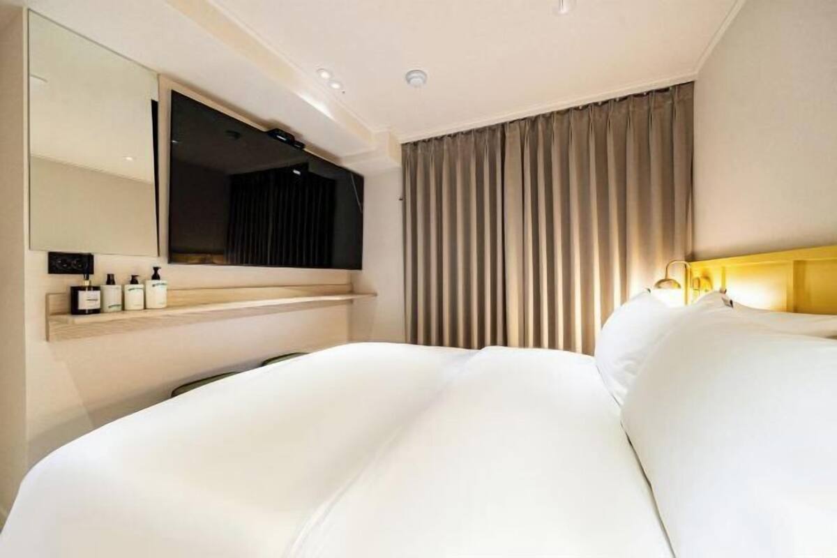 A hotel room with a large bed, a bedside table with toiletries, a mirror, and a window with curtains.