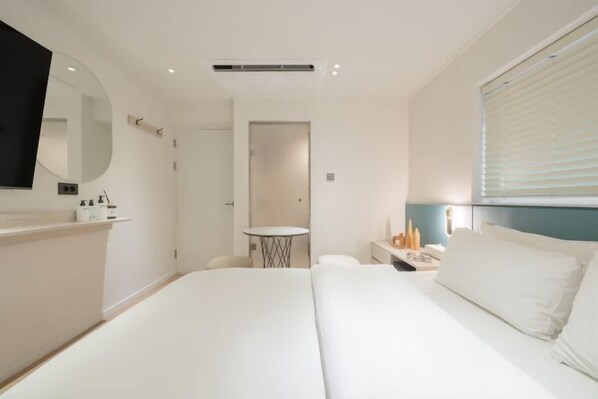 A hotel room with a large bed, a round mirror, a bedside table, a small round table, and a window with blinds. - Sinchon APL Hotel (Seoul)