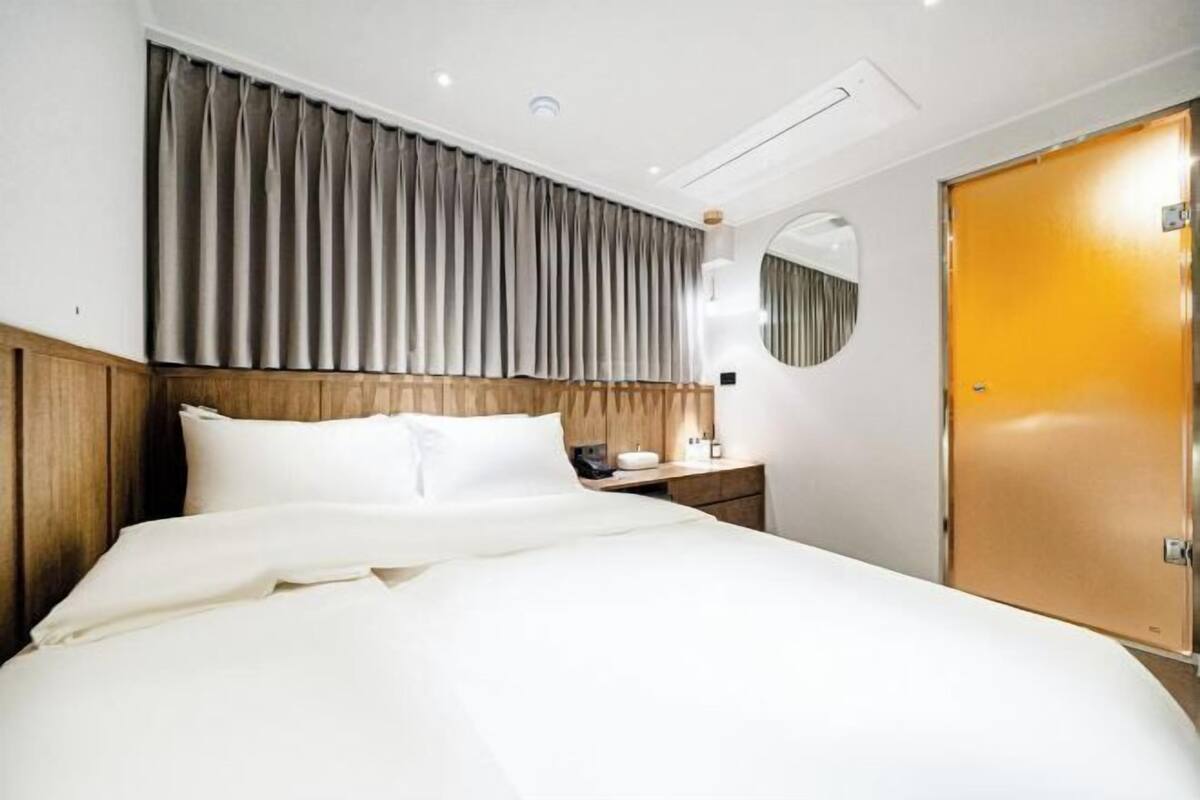 A hotel room with a bed, bedside table, lamp, and a door.