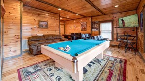Een houten interieur met een pooltafel, een bank en een televisie.