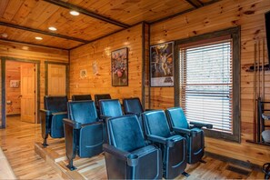 Une pièce aux murs et au plafond en bois, comprenant un coin salon avec des chaises et une fenêtre équipée de stores.
