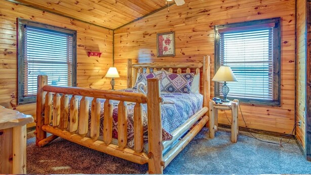 Een slaapkamer in een houten blokhut met een bed, twee bedlampen en een plafondventilator.