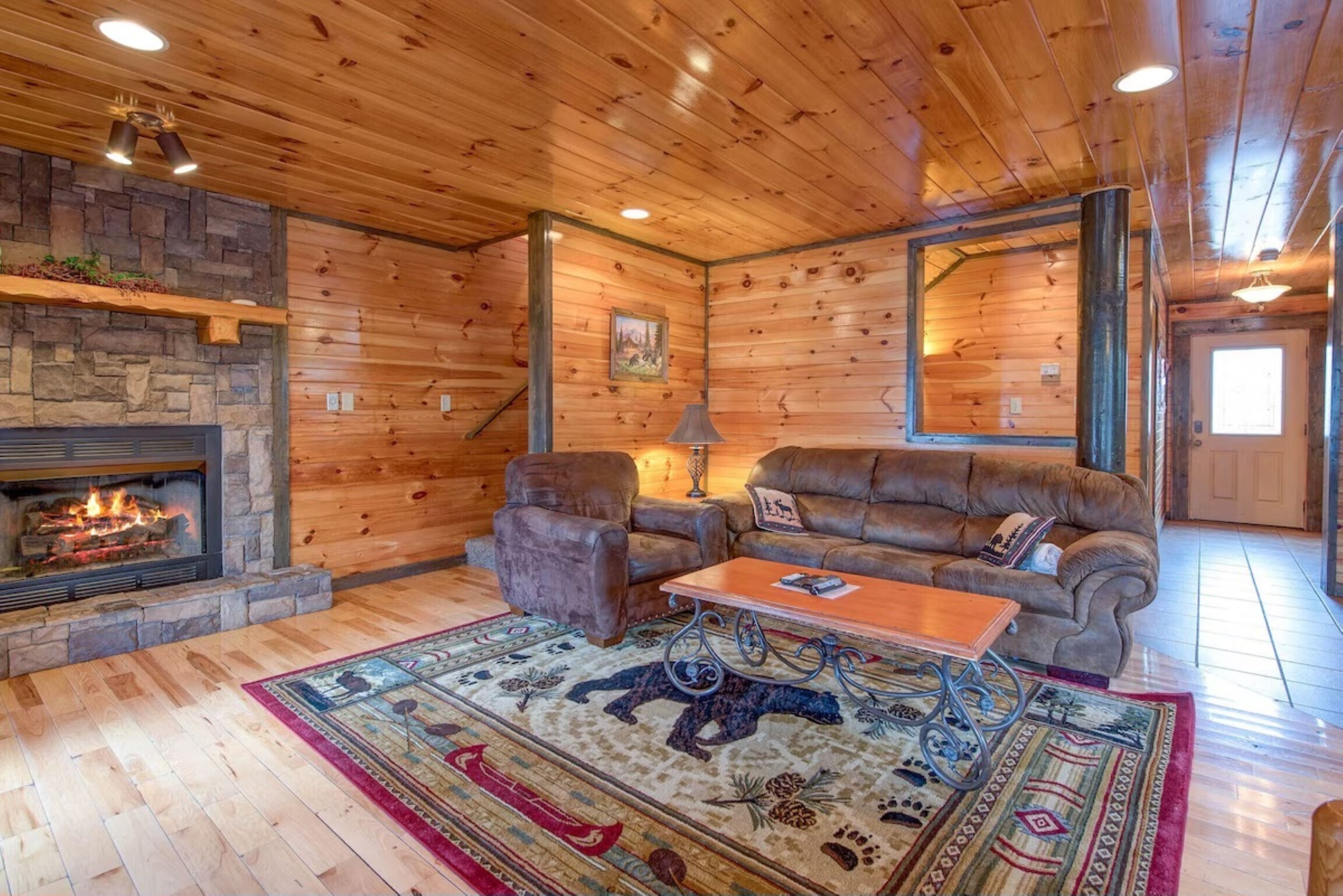 L’intérieur d’une cabane en rondins, avec une cheminée en pierre, des meubles en cuir et un grand miroir.